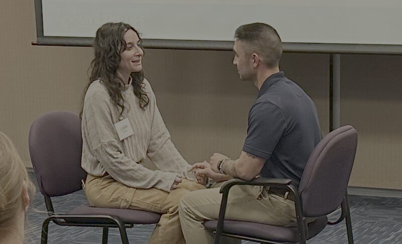 A couple sitting knee to knee, holding hands and talking during a workshop