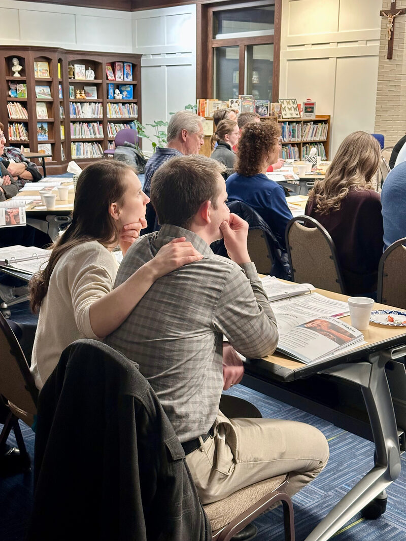Participants gathered around tables with workbooks during a parish session